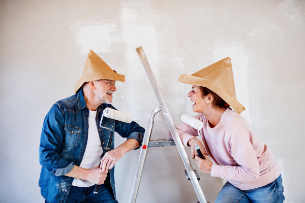 Portrait of cheerful senior couple painting walls in new home, having fun. Relocation concept.