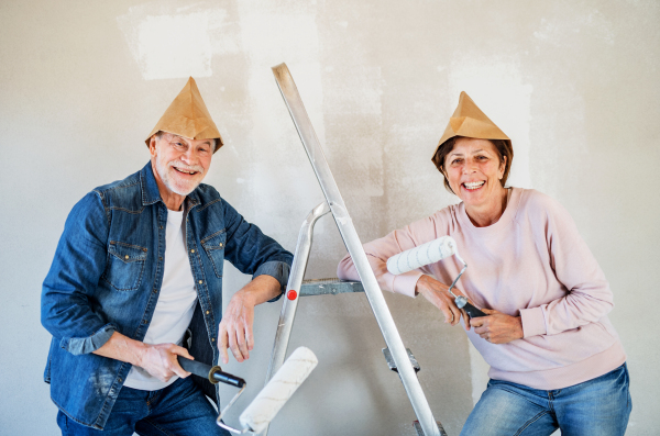 Portrait of cheerful senior couple painting walls in new home, having fun. Relocation concept.