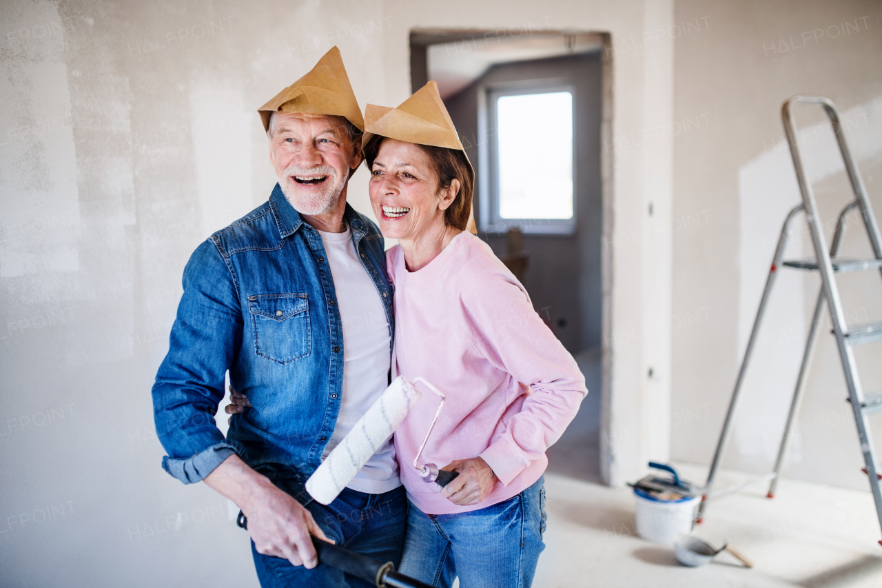 Portrait of cheerful senior couple painting walls in new home, laughing. Relocation concept.