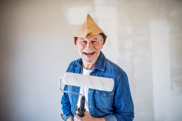 Portrait of cheerful senior man painting walls in new home, looking at camera. Relocation concept.