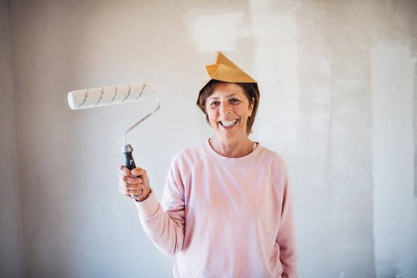 Portrait of cheerful senior woman painting walls in new home, having fun. Relocation concept.