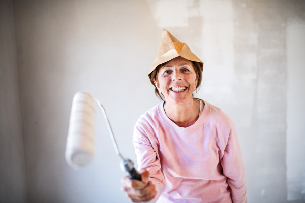 Portrait of cheerful senior woman painting walls in new home, having fun. Relocation concept.