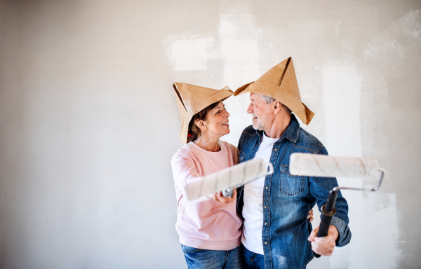 Portrait of cheerful senior couple painting walls in new home, having fun. Relocation concept.