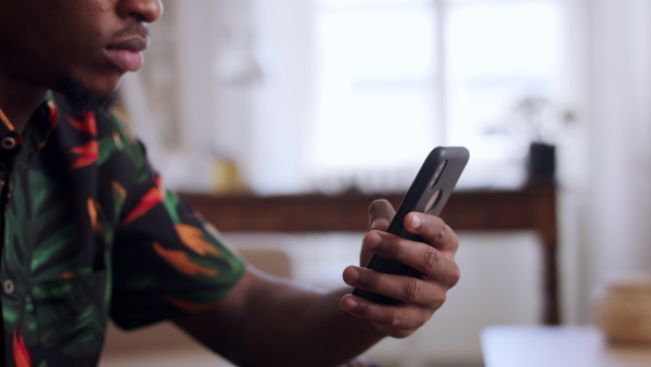 A close up of afro-american teenager sitting on sofa using smartphone. Social networks concept.