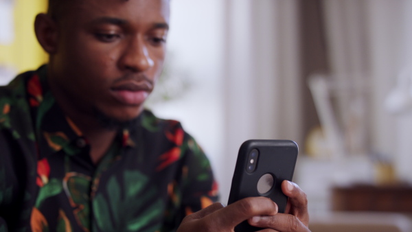 A close up of afro-american teenager sitting on sofa using smartphone. Social networks concept.