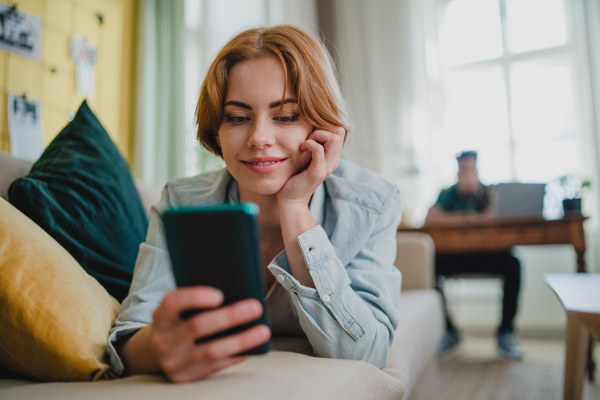 Happy young couple at home using digital divices, smartphone and laptop, socieal networks concept.