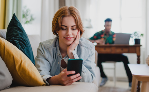 Happy young couple at home using digital divices, smartphone and laptop, socieal networks concept.