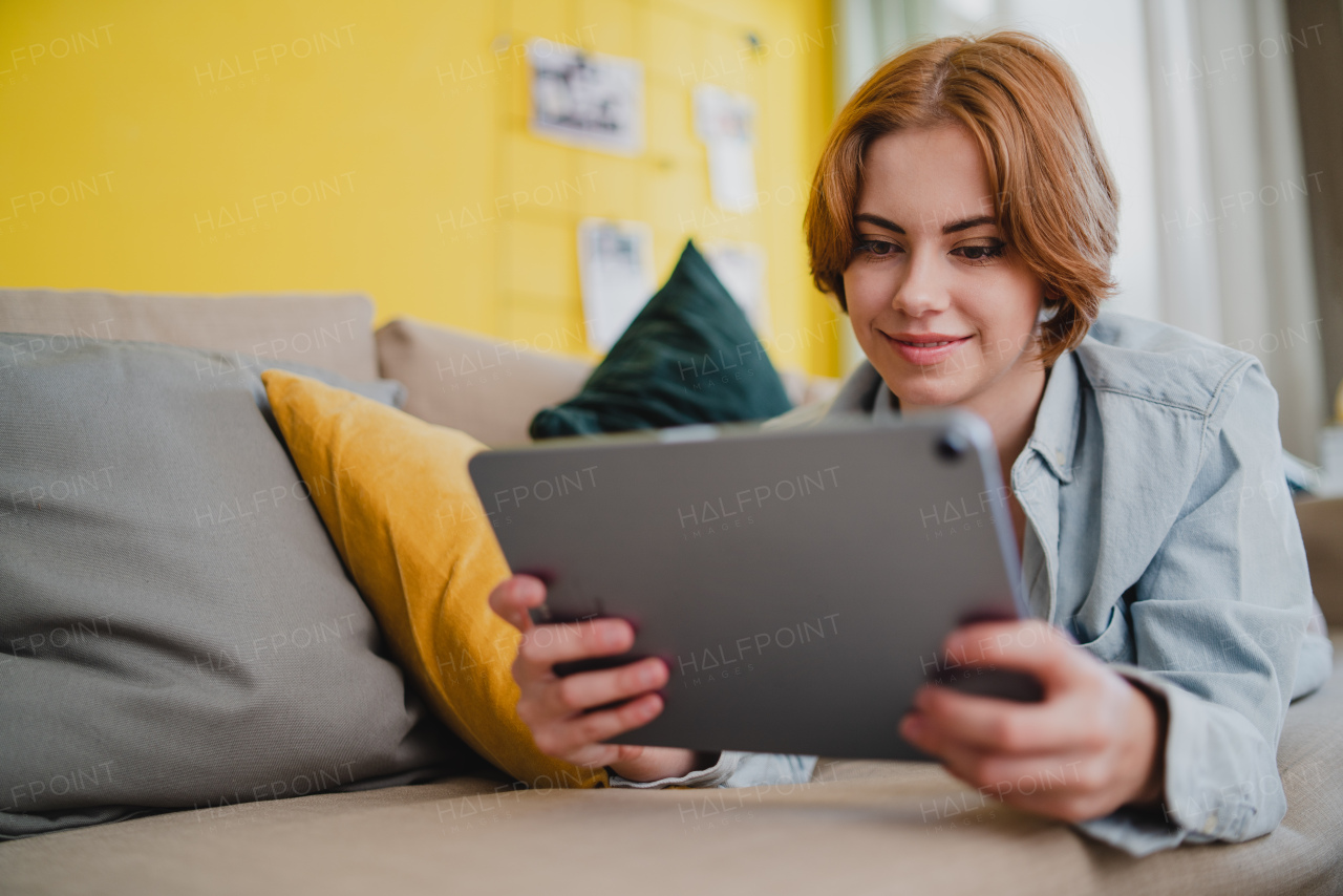 Portrait of a young woman using tablet, lying on sofa at home, social networks concept.