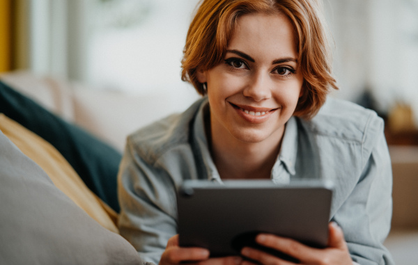 Portrait of a young woman using tablet, lying on sofa at home, social networks concept.