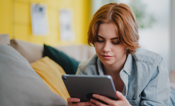 Portrait of a young woman using smartphone, lying on sofa at home, social networks concept.