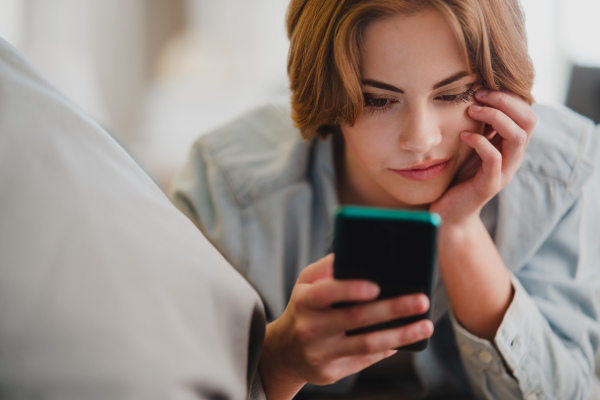 Portrait of a young woman using smartphone, lying on sofa at home, social networks concept.