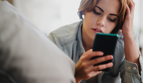 Portrait of a young woman using smartphone, lying on sofa at home, social networks concept.