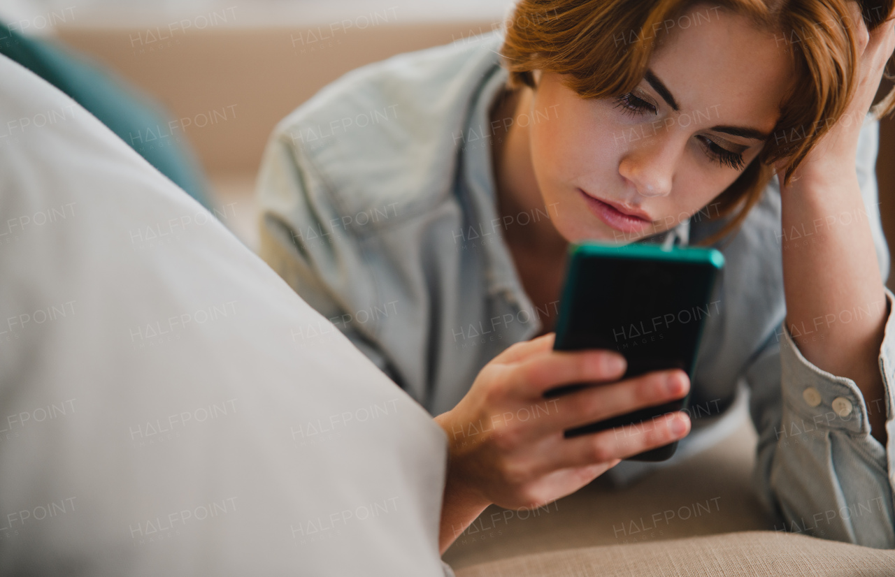 Portrait of a young woman using smartphone, lying on sofa at home, social networks concept.