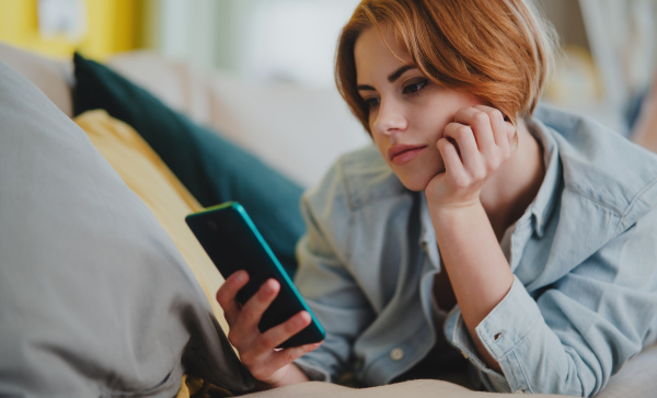 Portrait of a young woman using smartphone, lying on sofa at home, social networks concept.