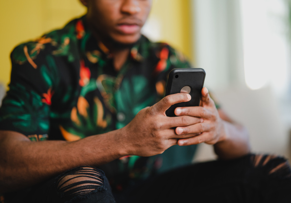 Portrait of an unrecognizable young man using smartphone, sitting on sofa at home, social networks concept.