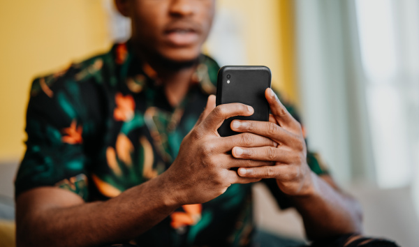 Portrait of an unrecognizable young man using smartphone, sitting on sofa at home, social networks concept.