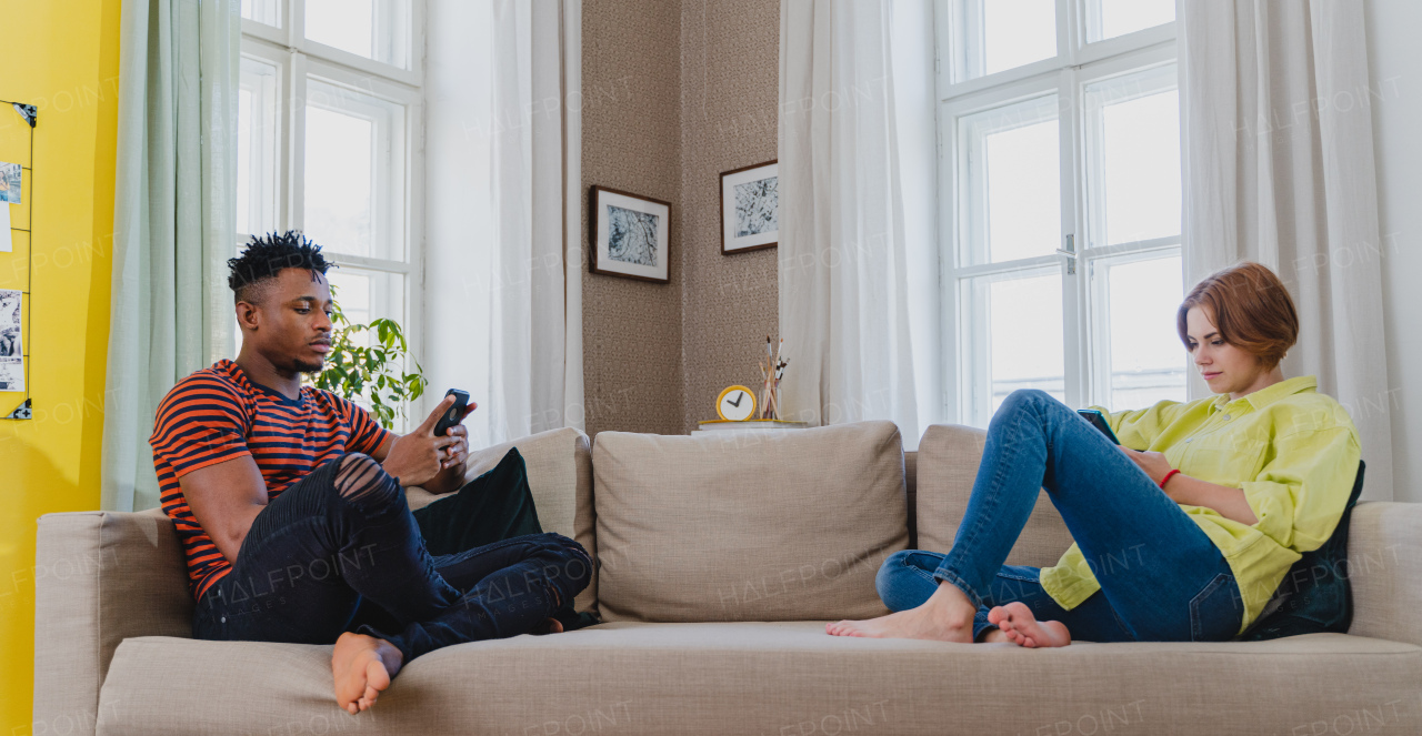 Young mixed couple addicted to smartphones sitting on a sofa at home.