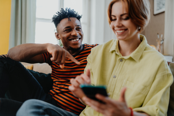 A young biracial couple using smartphone, having fun at home, checking social networks together.