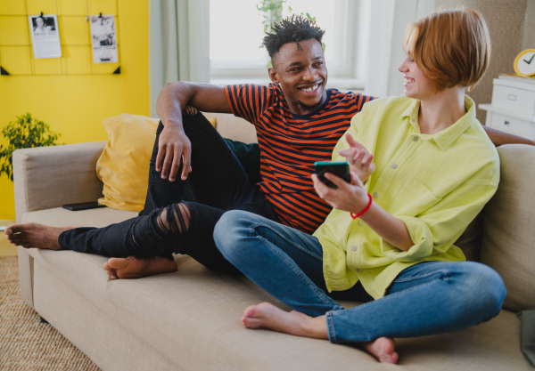 A young biracial couple using smartphone, having fun at home, checking social networks together.