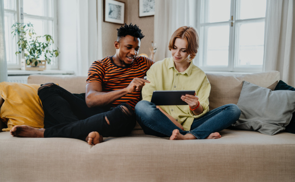 Young biracial couple using a tablet, having fun at indoors at home, checking social networks together.