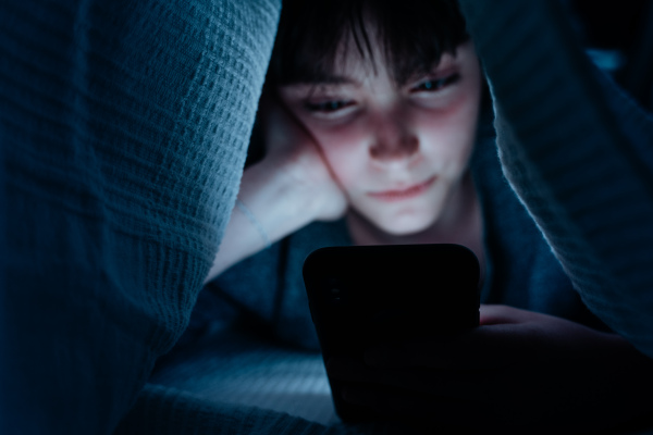 Teen girl using a smartphone, hiding under blanket at nigh, social networks cocnept.