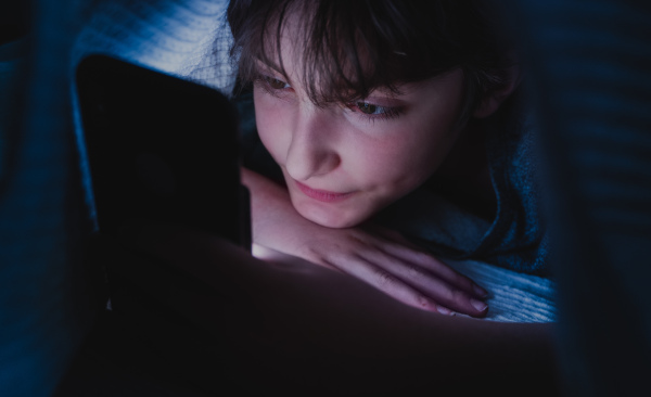 A happy teen girl using smartphone, hiding under blanket at nigh, social networks cocnept.