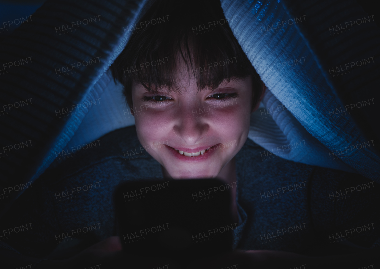 A happy teen girl using smartphone, hiding under blanket at nigh, social networks cocnept.