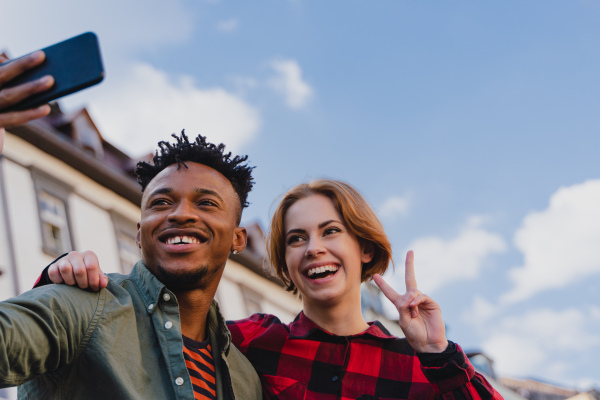 A low angle view of young biracial couple making selfie for soial networks outdoors in town.