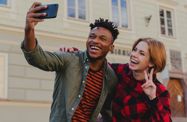 Young biracial couple making selfie for soial networks outdoors in a town.