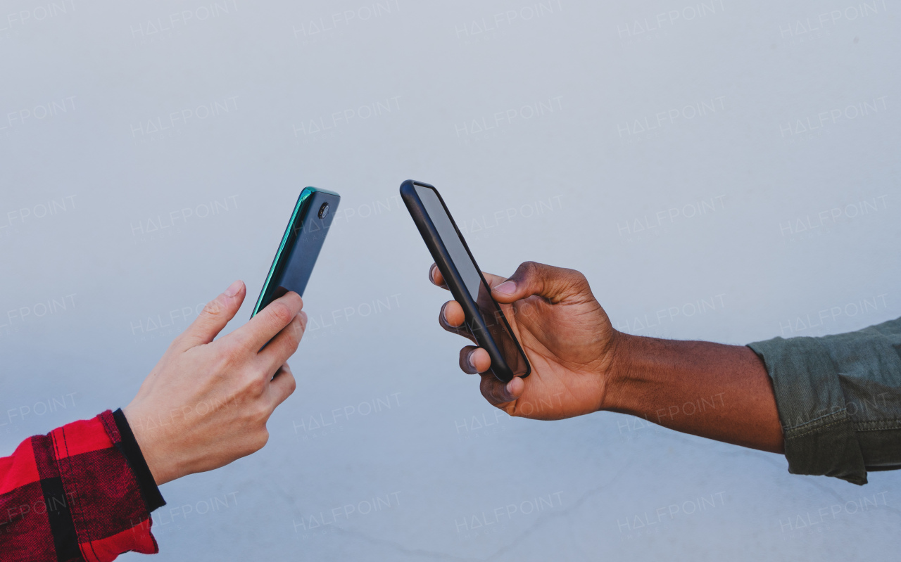 A close up of young biracial couple hands using smartphones on white background