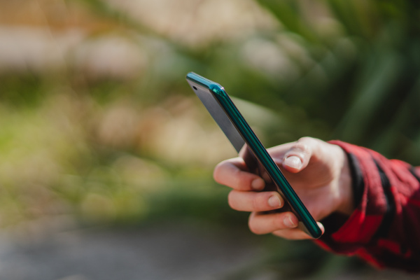 A close up of woman hand using smartphone, outdoors in park. Copy space.