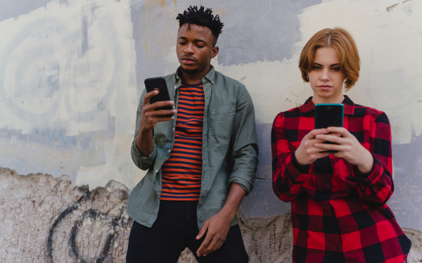 Young biracial couple addicted to smartphones outdoors in a town, social media concept