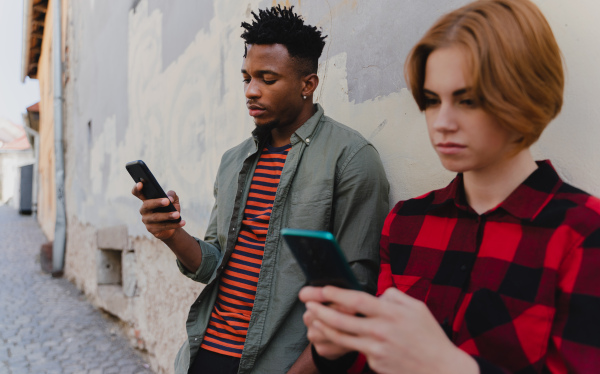 Young biracial couple addicted to smartphones outdoors in a town, social media concept