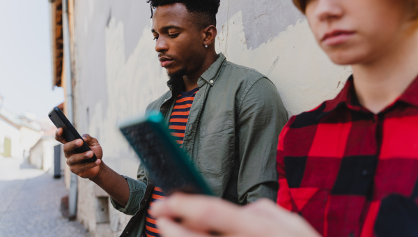 A young mixed couple using smartphones outdoors in town.