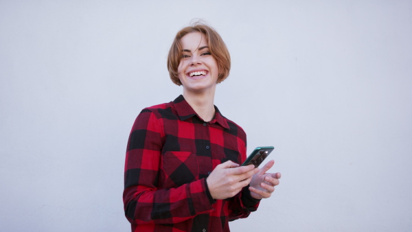 A front view of cheerful teenager standing, using smartphone and looking at camera. Social networks concept.