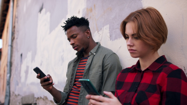 A side view of teenagers using smartphones and looking at camera. Social networks concept.