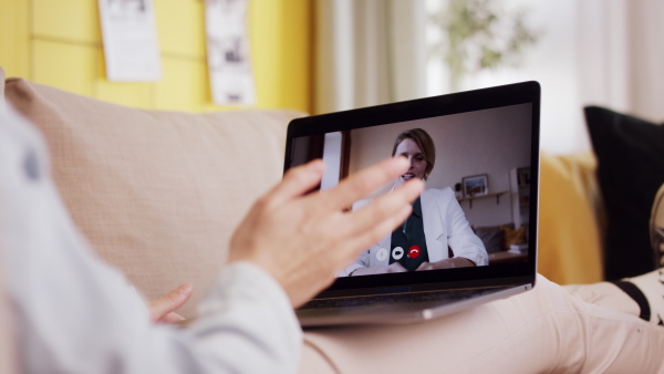 A rear view of teenager sitting on sofa, having a medical consultation on laptop. Social networks concept.