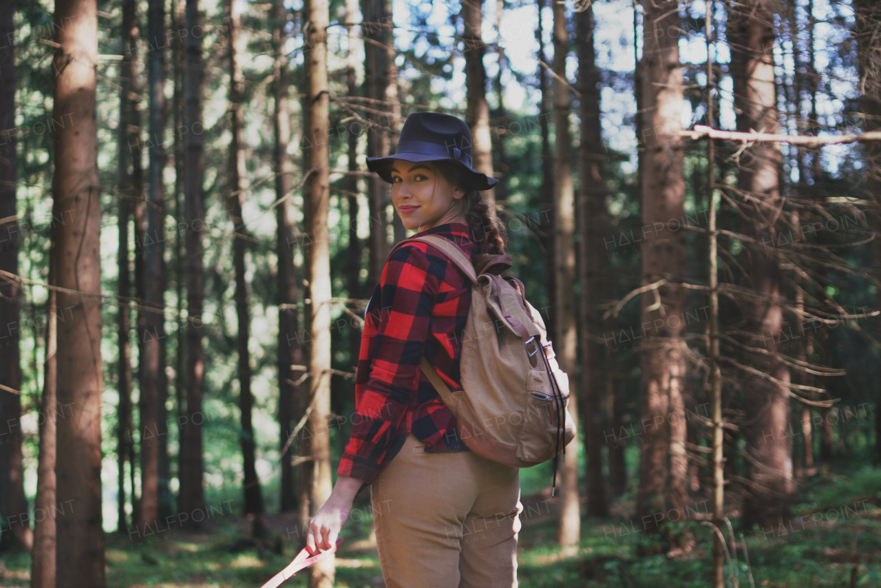 Young woman on a walk outdoors in forest in summer nature, looking back.