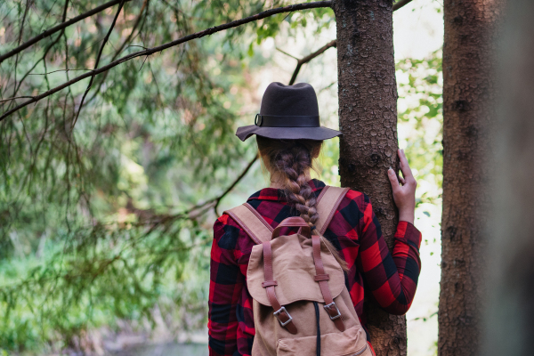 Rear view of young woman on a walk outdoors in forest in summer nature, standing.