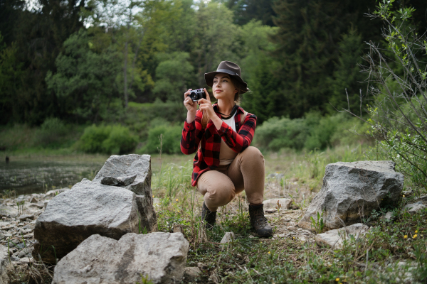 Front view of young woman with a dog on a walk outdoors in summer nature, taking photographs.