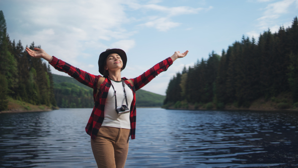 Young woman with closed eyes standing by lake on a walk outdoors in summer nature, relaxing.