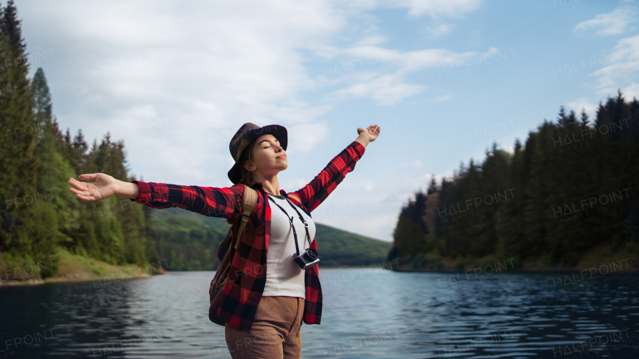 Young woman with closed eyes standing by lake on a walk outdoors in summer nature, relaxing.