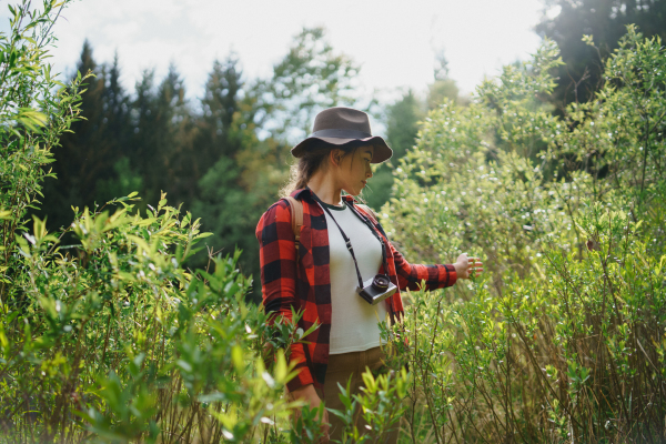 Front view of young woman with camera on a walk in forest in summer nature.