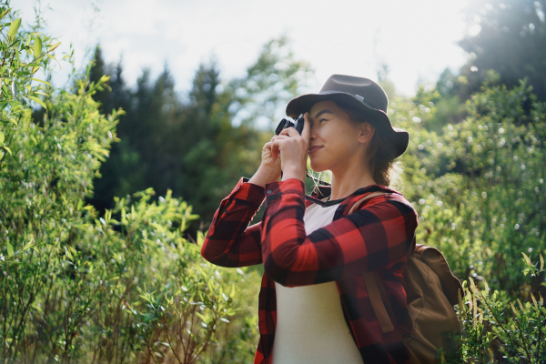 Side view of young woman with a dog on a walk outdoors in summer nature, taking photographs.