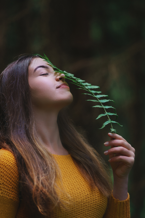 Close-up portrait of young woman on a walk outdoors in forest in summer nature, holding fern.