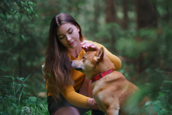 Happy young woman with a dog on a walk outdoors in summer nature.