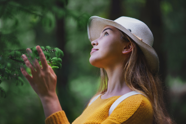 Side view of young woman on a walk outdoors in forest in summer nature, daydreaming.