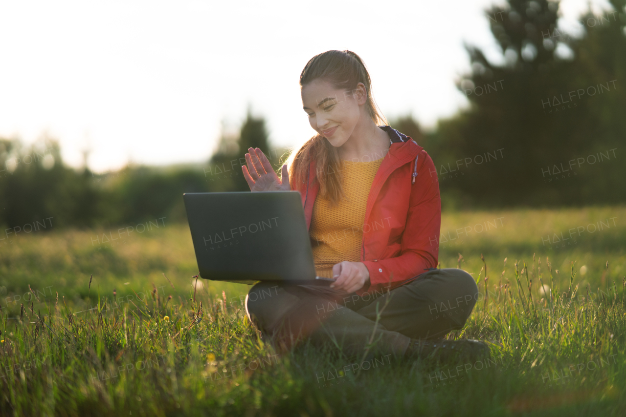 A happy young woman using laptop outdoors in summer nature, video call concept.