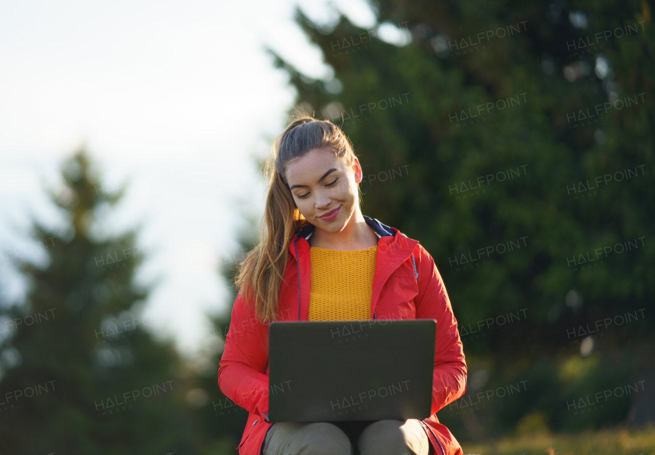 Front view of happy young woman using laptop in summer nature, outdoor office concept.