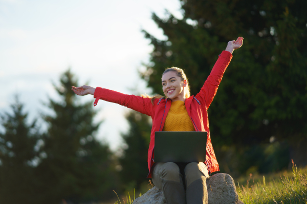 Front view of happy young woman using laptop in summer nature, outdoor office concept.